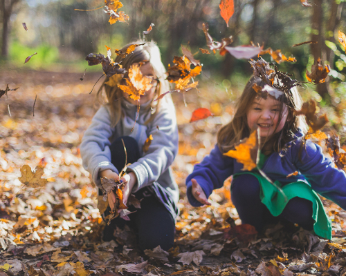 Shop Kids. Image description: Two young girls playing in fallen leaves. 